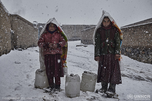 Refugees standing outside their tents in the snow when UNHCR assistance arrived to their settlement