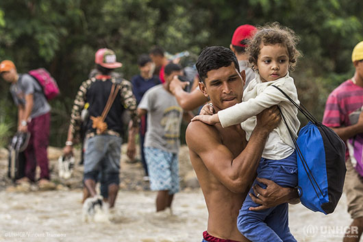 A father holds a young girl to cross the river and the border with Colombia.