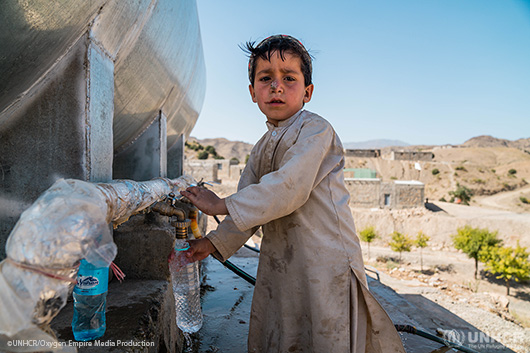 A young refugee child retrieving fresh drinking water from a tap